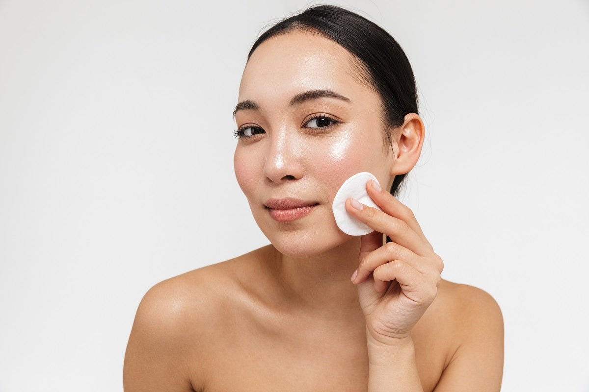 Beautiful young asian woman with healthy skin posing naked isolated over white wall background holding cotton pads.